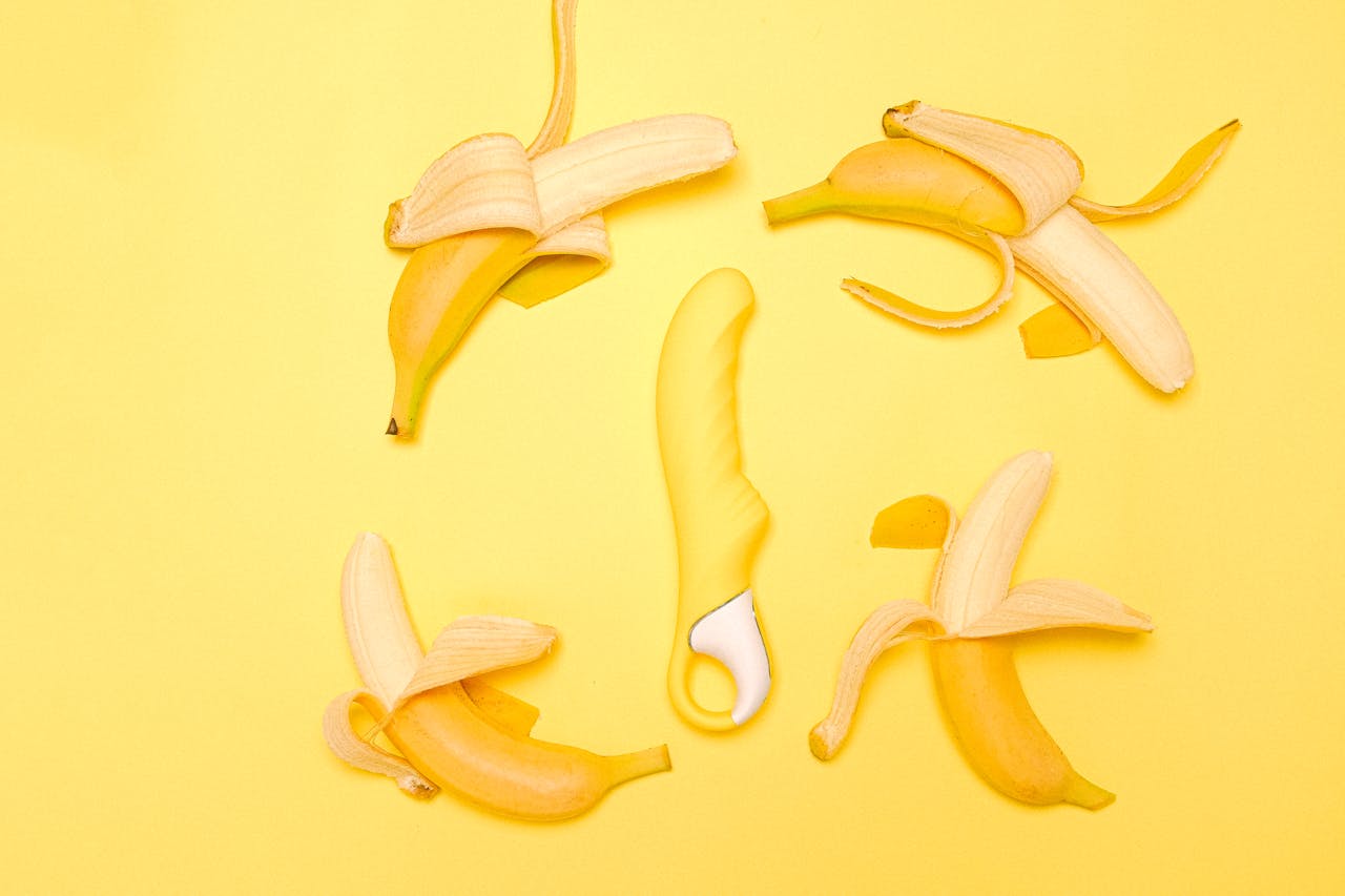 Home Creative flat lay of a yellow silicone vibrator surrounded by peeled bananas on a yellow background.