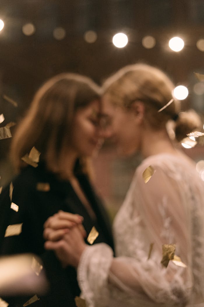 Home A romantic dance between two women, surrounded by golden confetti at a party event.