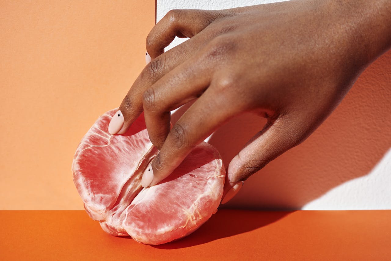 Home Close-up of a hand gently touching a grapefruit against an orange background, showcasing freshness and elegance.